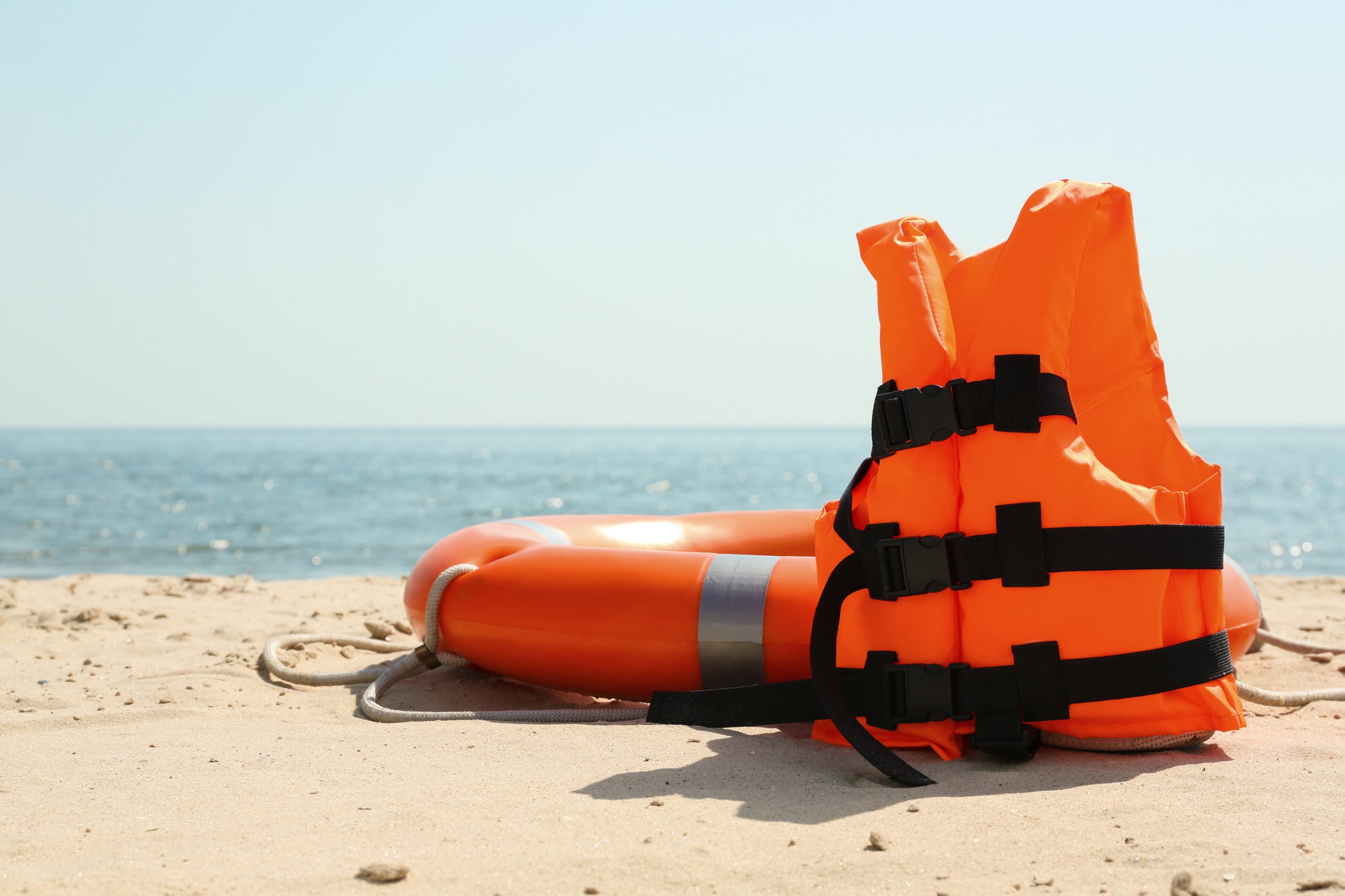 Orange life jacket and buoy on sandy beach near sea. Emergency rescue equipment