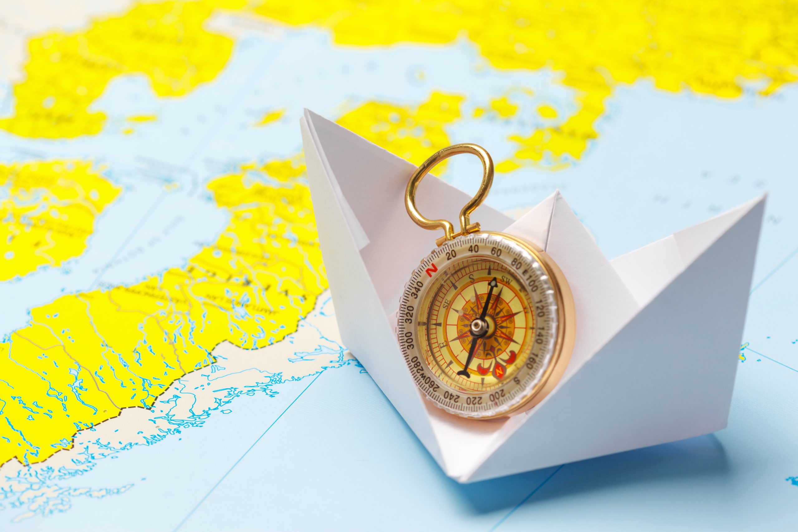 Paper boat with compass sailing on a colorful world map